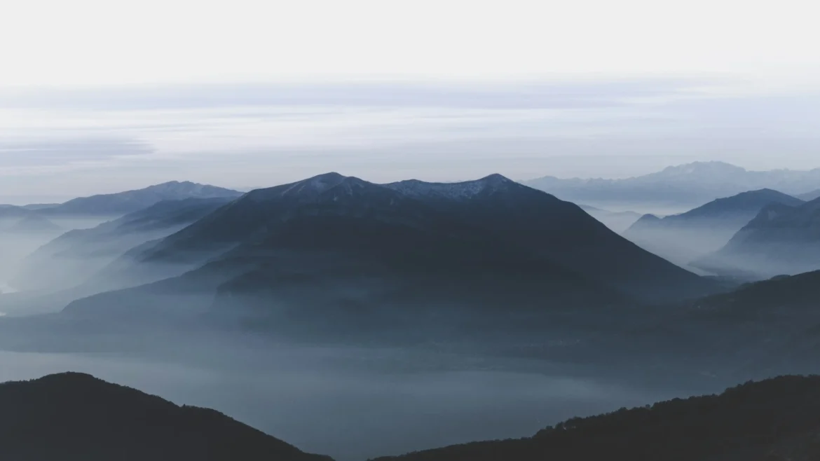 Misty mountain landscape with layered alpine peaks covered in morning fog under a peaceful blue sky in stunning 4K wallpaper