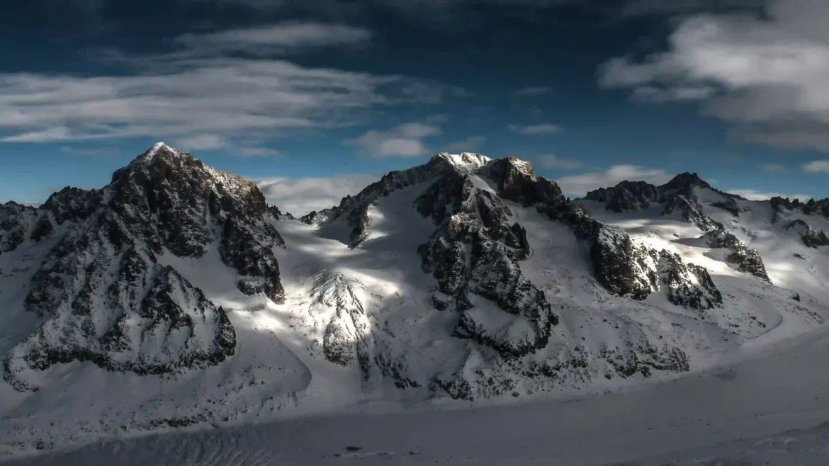 Snow-covered alpine mountain peaks with glaciers and dramatic clouds under a blue sky in a stunning 4K nature wallpaper
