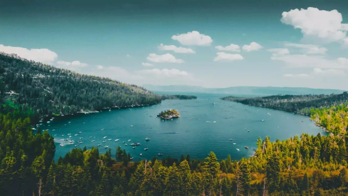 Aerial view of a blue alpine lake surrounded by evergreen forests and mountains with a small island at the center in an Ultra HD 4K nature wallpaper