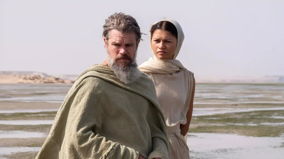 Matt Damon and Zendaya in ancient attire standing near a desert shoreline in a cinematic 4K wallpaper