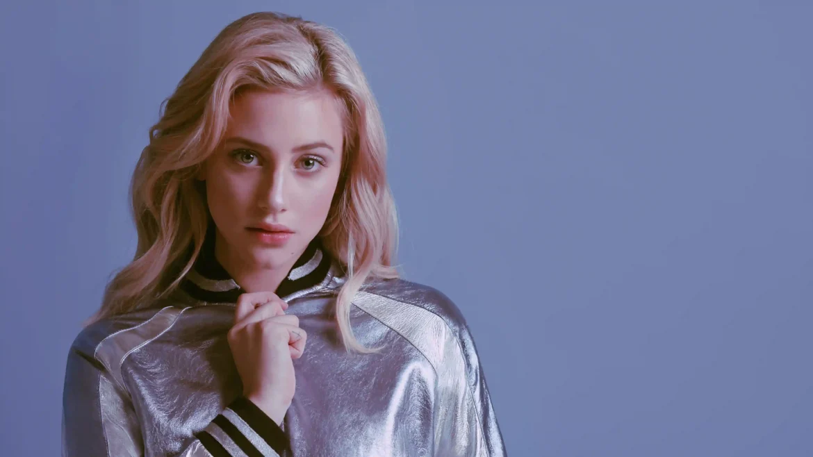 Actress Lili Reinhart wearing a metallic silver jacket looking at the camera against a slate blue background in a 4K wallpaper
