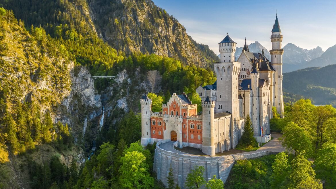 Aerial view of Neuschwanstein Castle nestled in lush green trees against the Bavarian Alps with Marienbrücke bridge in a 4K wallpaper