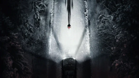Top-down view of a car on a snowy forest road at night with headlights illuminating a tall shadow figure in a 4K Resident Evil movie poster wallpaper