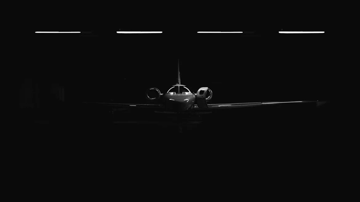 Minimalist dark photography of a luxury private jet head-on silhouette inside a black hangar lit by overhead strip lights in a 4K wallpaper